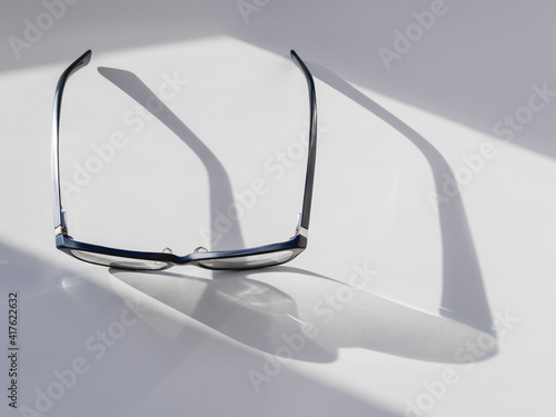 Top view of eyeglasses on white background. Comfortable life with poor eyesight. Ophthalmology. Contrast of hard sunlight and geometrical shadow. photo