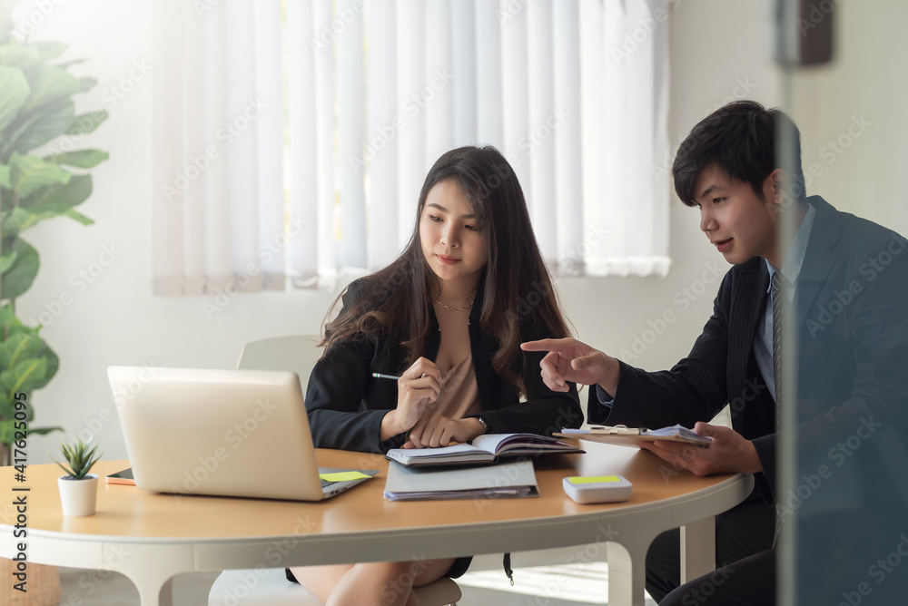 Obraz premium Asian businessman and businesswoman are working on collaboration ideas using laptop and taking note office.