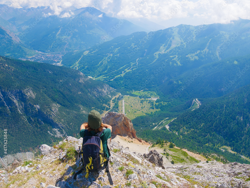 Woman with backpack resting on mountain top, looking at view dramatic landscape valley summer activity fitness wellbeing freedom concept, selective focus rear view