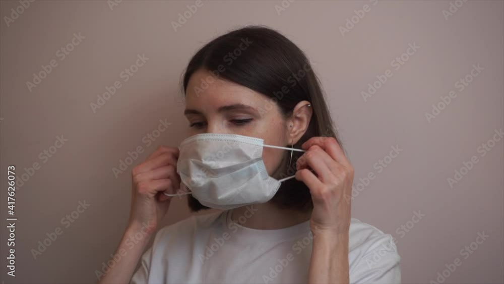 Social distancing and new normal. Close up portrait of young woman putting on protective medical mask, orange studio background, slow motion Social distancing and new normal. Close up portrait of young woman putting on protective medical mask, orange studio background, slow motion