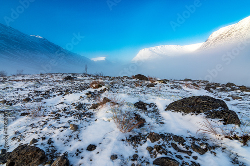 Fog in the mountains on a winter morning at sunrise. Mountain valley covered with snow in winter.