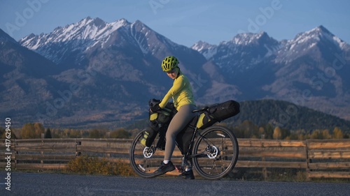 The woman travel on mixed terrain cycle touring with bikepacking. The traveler journey with bicycle bags. Sport tourism bikepacking  bike  sportswear in green black colors. Mountain snow capped.