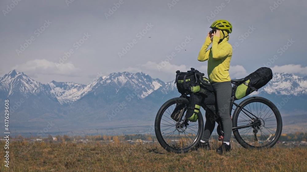 The woman travel on mixed terrain cycle touring with bikepacking. The traveler journey with bicycle bags. Sport tourism bikepacking, bike, sportswear in green black colors. Mountain snow capped. The woman travel on mixed terrain cycle touring with bikepacking. The traveler journey with bicycle bags. Sport tourism bikepacking, bike, sportswear in green black colors. Mountain snow capped.