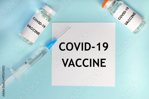 Covid-19 vaccine is written on a white sheet that lies on a blue background among ampoules and a syringe. Vaccination of the population