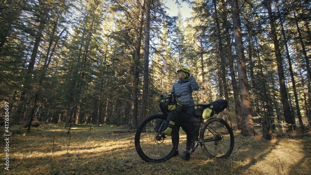 The woman travel on mixed terrain cycle touring with bike bikepacking outdoor. The traveler journey with bicycle bags. Stylish bikepacking, bike, sportswear in green black colors. Magic forest park.