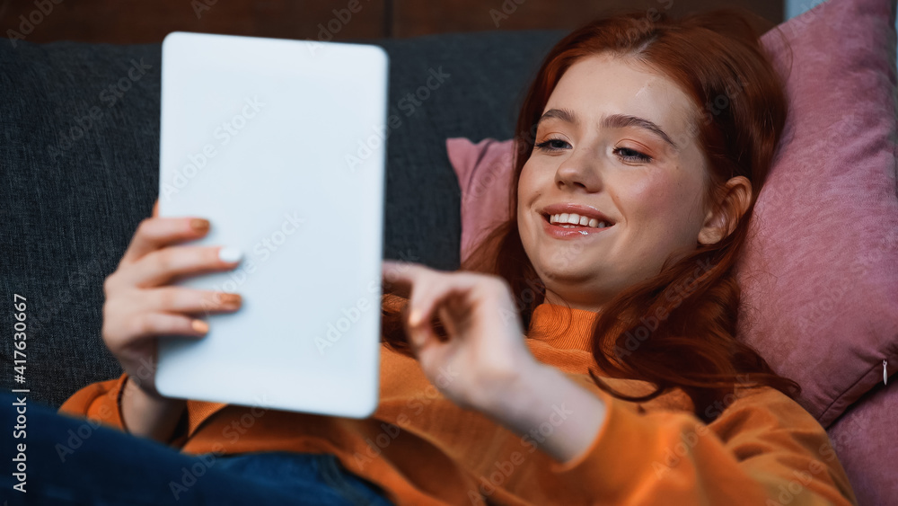 Smiling teenager using digital tablet on blurred foreground at home Smiling teenager using digital tablet on blurred foreground at home
