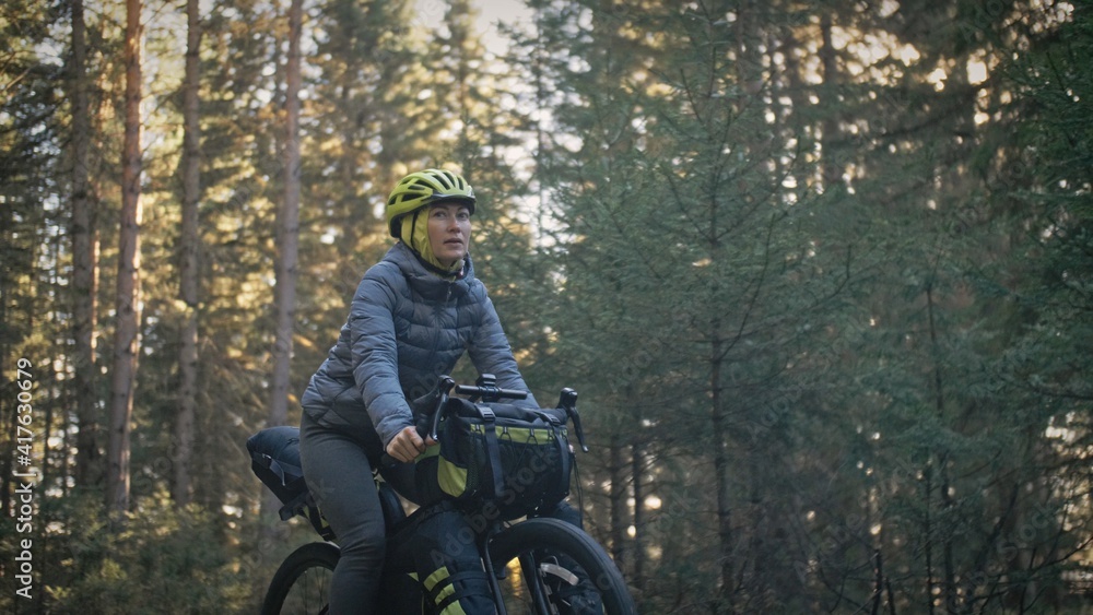 The woman travel on mixed terrain cycle touring with bike bikepacking outdoor. The traveler journey with bicycle bags. Stylish bikepacking, bike, sportswear in green black colors. Magic forest park. The woman travel on mixed terrain cycle touring with bike bikepacking outdoor. The traveler journey with bicycle bags. Stylish bikepacking, bike, sportswear in green black colors. Magic forest park.