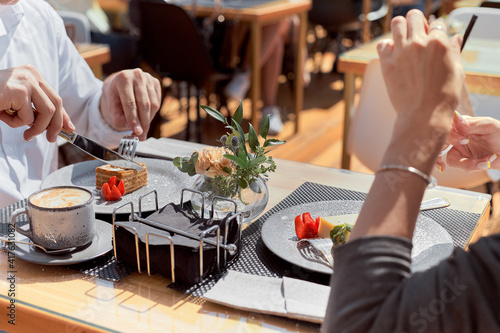 Young couple in a cafe eating coffee and dessert. Close-up of hands and bowl with dessert.
