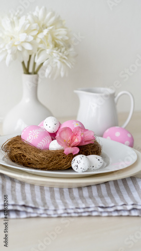 Easter lunch. Festive menu. Holiday food decoration. Party catering. Pink color painted eggs in nest served in plate with white Spring flower bouquet tablecloth composition on light background.