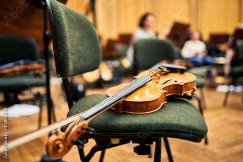 A close-up of a wooden violin, lying on a chair. The rehearsal room in the background.