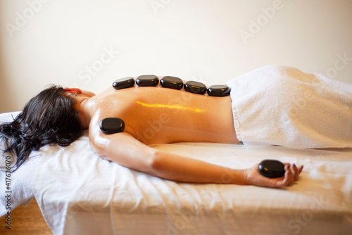 Hot stone massage, stone therapy, Thai massage, relaxation retreat, healing procedure, a girl with a bare back lies, black stones in her hands