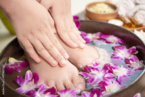 closeup view of woman soaking her hand and feet in dish with water and flowers on wooden floor. Spa treatment and product for female feet and hand spa. orchid flowers in ceramic bowl. © nareekarn
