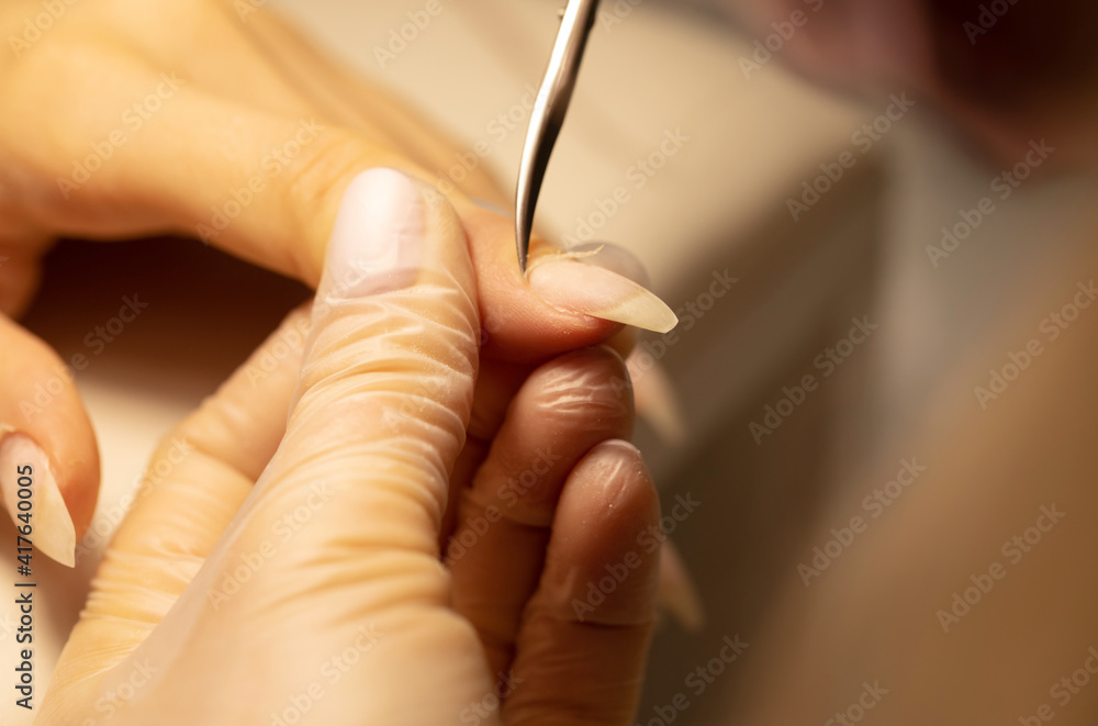 Close up of manicurist hands clipping client nails. Young woman getting manicure treatment. Clipping nails, hand care and nail care at beauty salon. Selective focus.