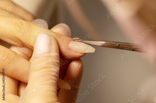 Close up of manicurist hands clipping client nails. Young woman getting manicure treatment. Clipping nails  hand care and nail care at beauty salon. Selective focus.