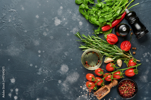 Food cooking background. Fresh rosemary, cilantro, basil, cherry tomatoes, peppers and olive oil, spices herbs and vegetables at black slate table. Food ingredients top view.