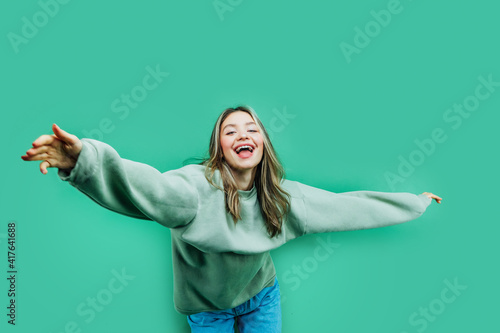 Joyful girl reaches for the camera, she is dancing with her hands on a green background, next to her is a place for a text, an inscription for a discount © Тарас Нагирняк