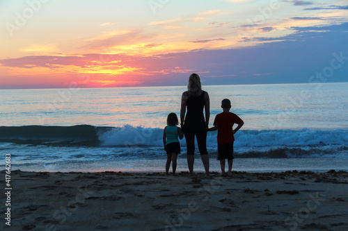Silhouette of Mother with daughter and son watching sunrise along the beach of the Atlantic Ocean off barrier island of The Outer Banks, North Carolina photo