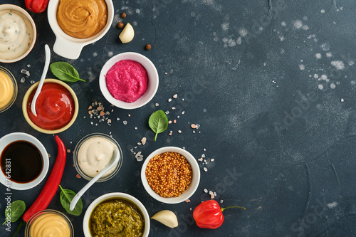 Set of sauces in bowls - ketchup, mayonnaise, mustard, soy sauce, bbq sauce, pesto, chimichurri, mustard grains on dark stone background. Top view copy space.