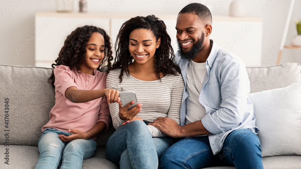 Happy african american family holding and using smartphone