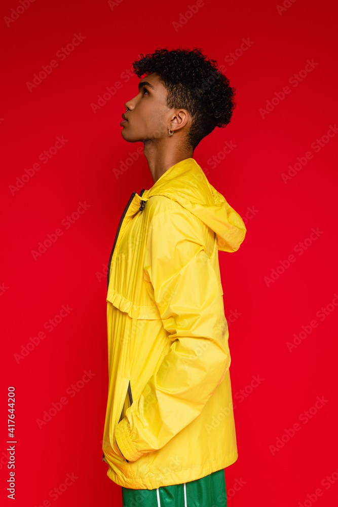 side view of african american man in yellow jacket posing isolated on red side view of african american man in yellow jacket posing isolated on red