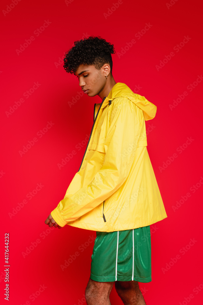 african american man in jacket and shorts posing on red