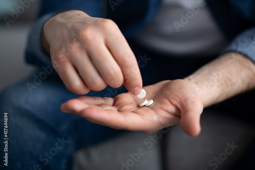 Unrecognizable man holding couple of pills, closeup