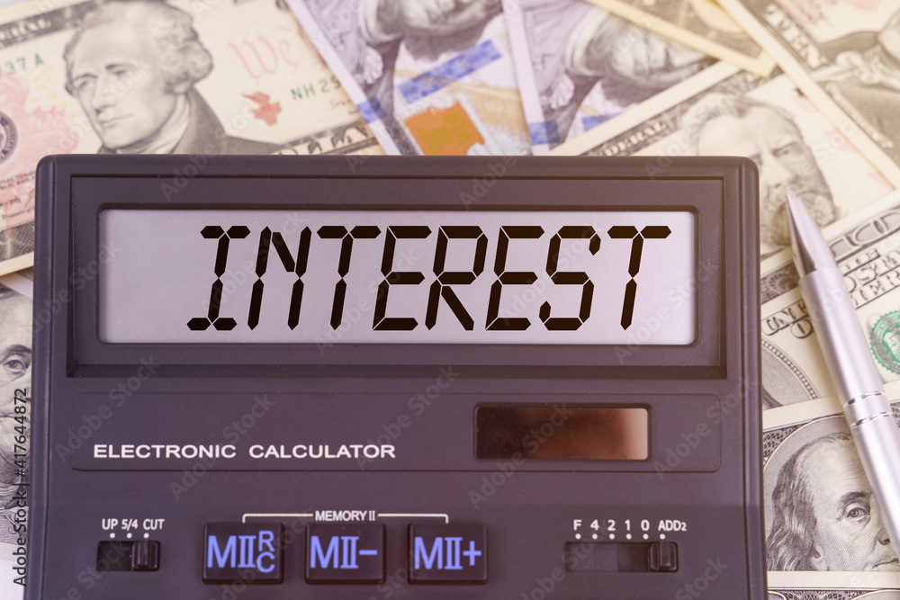 On the table are dollars and a calculator on the electronic board which says INTEREST On the table are dollars and a calculator on the electronic board which says INTEREST