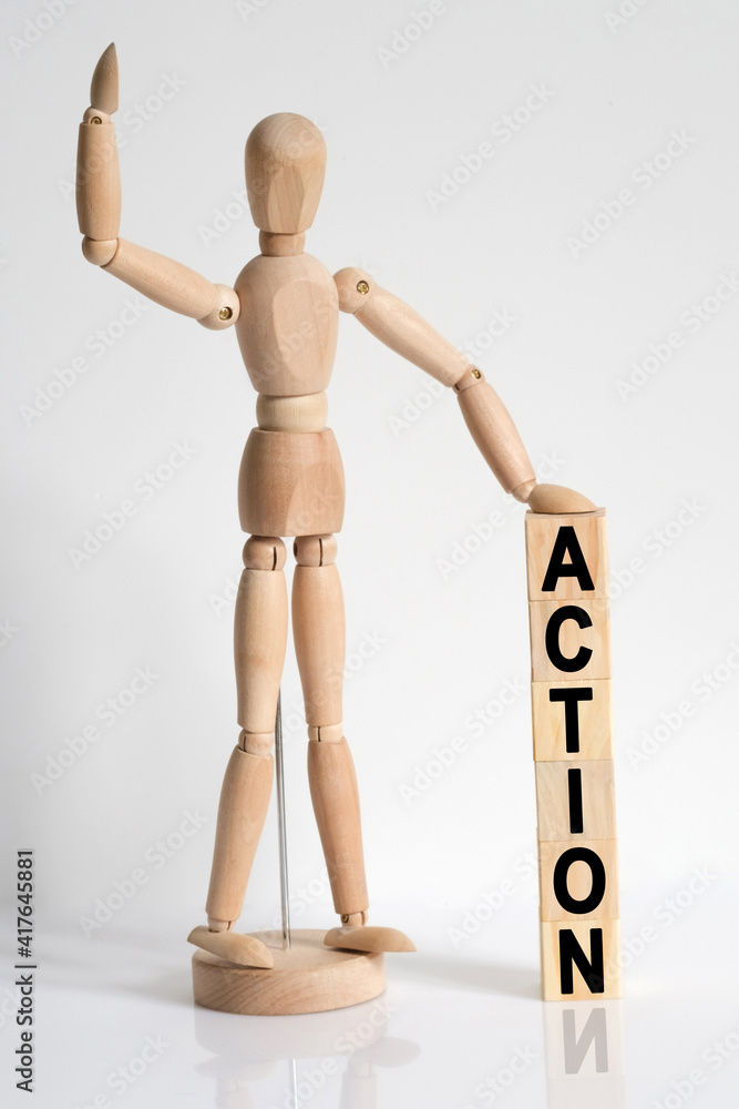 The wooden man raised his hand, and under his left hand he has cubes with the inscription - ACTION The wooden man raised his hand, and under his left hand he has cubes with the inscription - ACTION