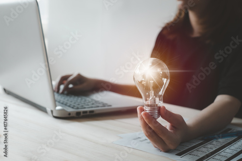 woman hand holding lightbulb with using laptop or compter notebook for working job. idea Thinking differently creates inspiration for working in office  New innovations and technologies concept. photo