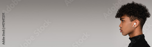 side view of african american man listening music in wireless earphones isolated on grey, banner