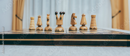 Figuras de ajedrez de madera blanca sobre tableo, en el centro la reina blanca la rodean caballos, alfiles y torres simétricamente. photo