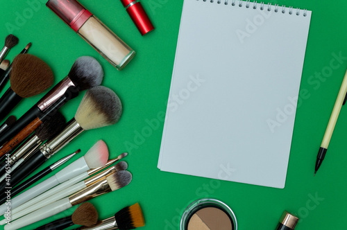 Make up the essentials. A set of professional makeup brushes and cosmetics on a green background. Next to it is a notebook with a pencil. Perfect for a beauty blog. Flatly, horizontal.