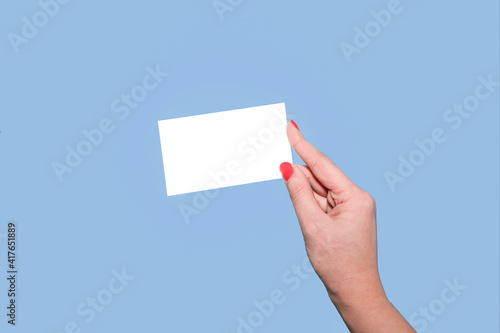 Female hand with red manicure, with mock-up paper, business card or discount card on a blue background. copy space for text