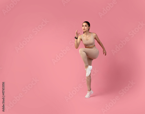 Fototapeta Naklejka Na Ścianę i Meble -  Young Woman Doing High Knees Exercise Isolated On Pink Background