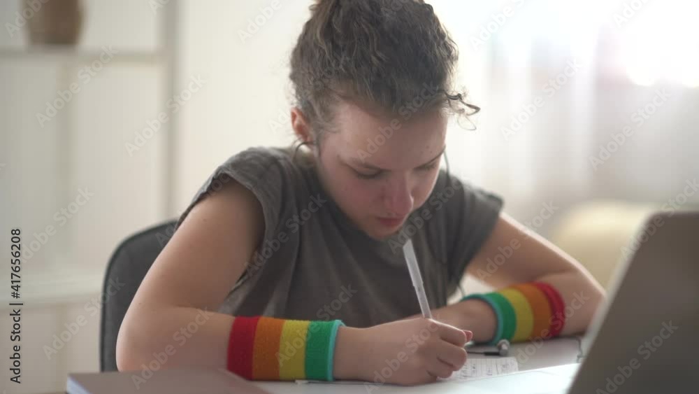 Curly-haired teenager girl makes homework near the laptop. Online learning, distance learning, home schooling Curly-haired teenager girl makes homework near the laptop. Online learning, distance learning, home schooling