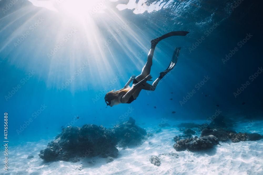 Woman freediver glides with fins. over sandy sea. Freediving and beautiful sunlight in ocean