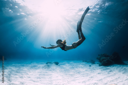 Woman freediver glides with fins. over sandy sea. Freediving and beautiful sunlight in ocean