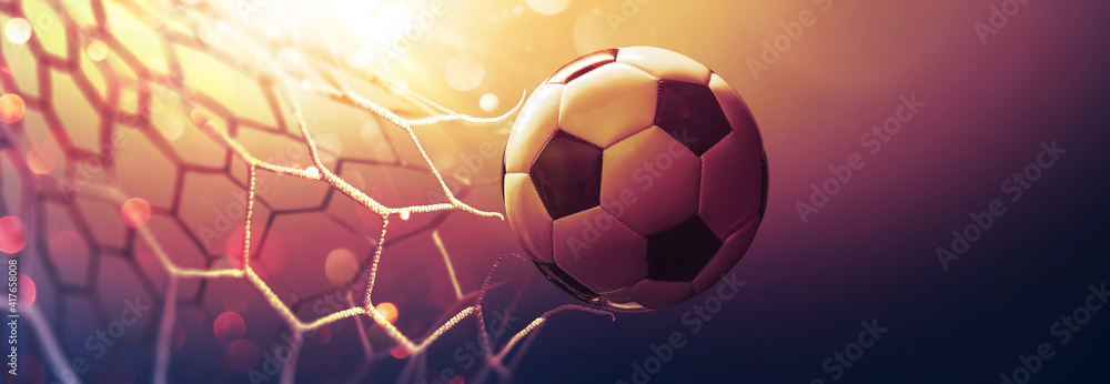 Soccer ball in the net in the sunbeams. Golden background