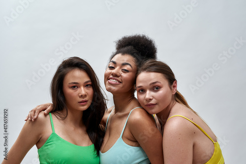 Studio portrait of three confident multiethnic women in colorful underwear posing together isolated over light background