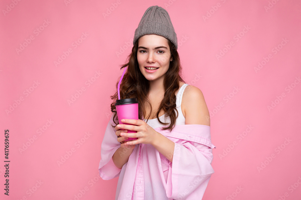 Beautiful young positive brunette woman wearing casual stylish clothes isolated over colorful background wall holding paper cup for mockup drinking coffee looking at camera Beautiful young positive brunette woman wearing casual stylish clothes isolated over colorful background wall holding paper cup for mockup drinking coffee looking at camera