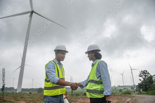 Two engineers working and holding the report at wind turbine farm Power Generator Station on mountain,Thailand people