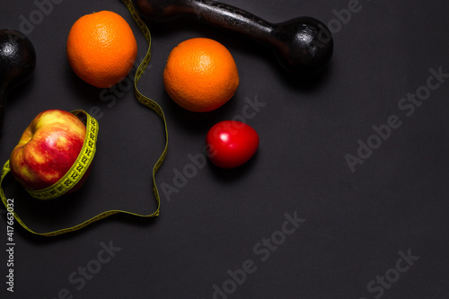 Creative flat lay of fitness equipment and fruits and vegetables on the black. Healthy lifestyle concept. Copy space. Apple with a tape measure, summer body concept