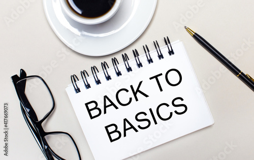 Glasses, a white cup of coffee, a white notebook with the words BACK TO BASICS and a ballpoint pen lie on a light background. Flat lay. View from above.