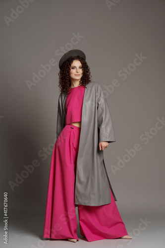 Studio shot of curly fashion model in bright pink clothes and leather jacket on gray background with copy space