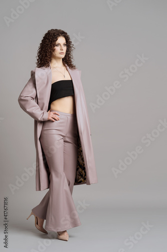 Studio shot of pretty fashion model in pastel purple leather trousers and coat on gray background