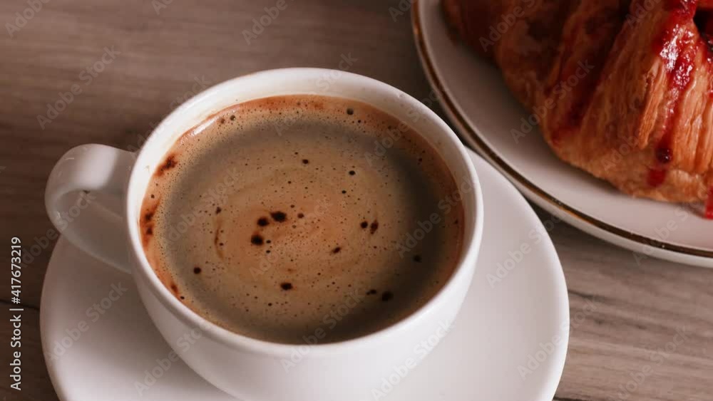 Espresso coffee in a white cup and one croissant over light wooden table background. Espresso coffee in a white cup and one croissant over light wooden table background.
