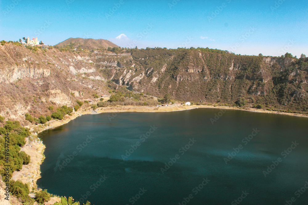 Un enorme lago, con forma de crater volcanico en un pueblo pequeño con fondo de dos montañas