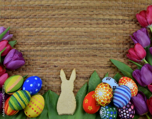 tulips, painted eggs and bunny shaped cookies on brown background photo