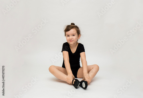 little gymnast girl in a black uniform does a stretch on a white background with a place for text