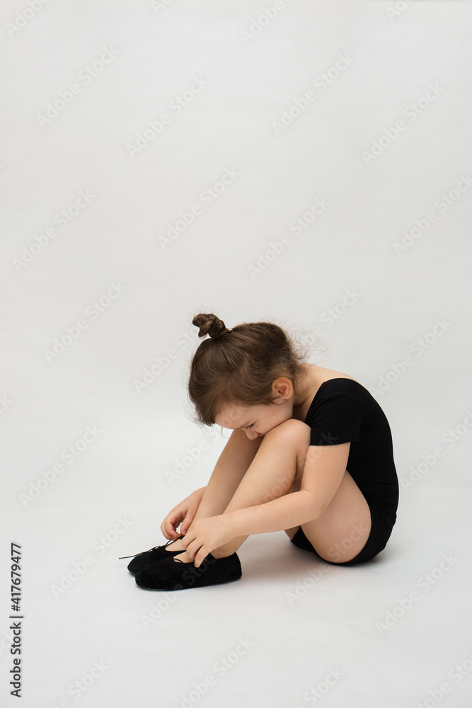 Fototapeta premium little gymnast girl sits on a white background with space for text